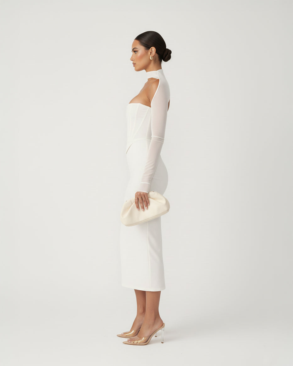Woman in a white dress holding a matching clutch against a plain background