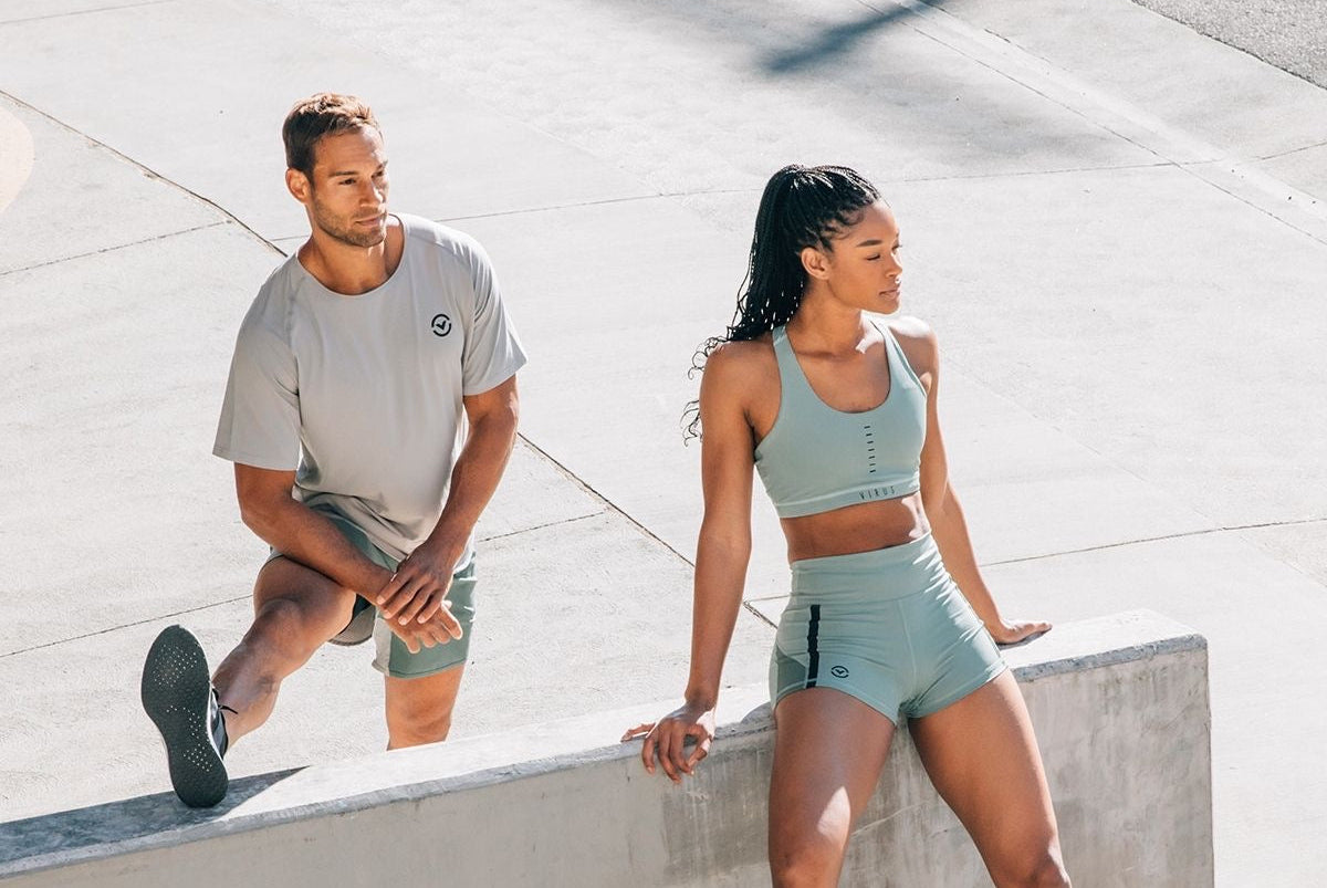 Two people in athletic wear sitting on a concrete ledge outdoors.